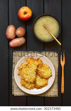 Homemade potato pancakes or fritters on plate with apple sauce, a traditional dish in Germany, photographed overhead on dark wood with natural light