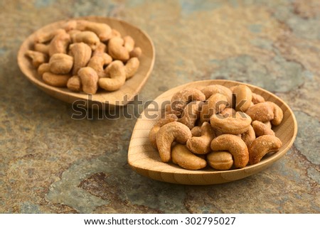 Salted cashew nuts or seeds on small bamboo plates, photographed on slate with natural light (Selective Focus, Focus on the first cashews on the right plate)