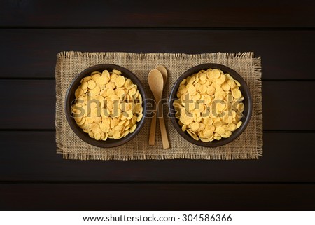 Crispy corn flakes breakfast cereal in rustic bowls with small wooden spoons, photographed overhead on dark wood with natural light