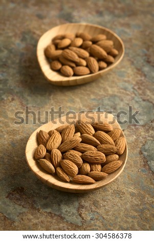 Shelled almonds with seedcoat on small bamboo plates, photographed on slate with natural light (Selective Focus, Focus one third into the almonds on the first plate)