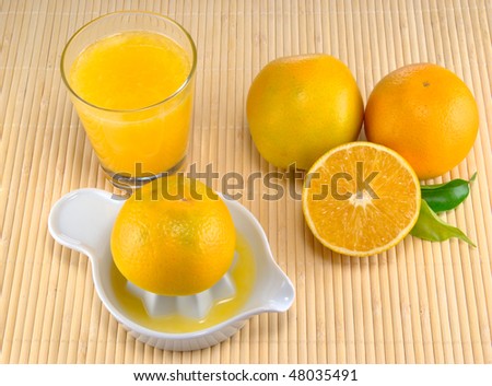 Fresh orange juice on a table mat with squeezer and oranges