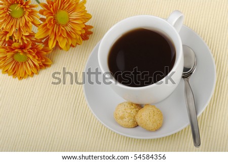 Black tea in cup with saucer, teaspoon, biscuits and orange flower in the background on table mat (Selective focus)