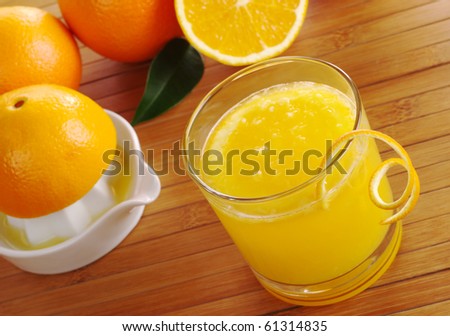Fresh orange juice with orange slice in glass with squeezer and oranges in background on table mat (Selective Focus)