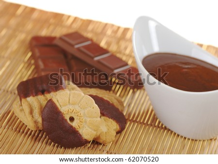 Butter cookies dipped in milk chocolate icing with chocolate dip in white bowl and chocolate bar on table mat (Selective Focus)
