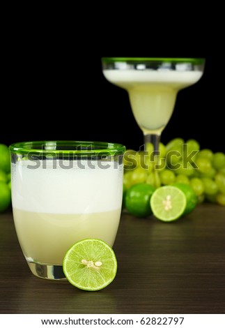 Pisco Sour, a Peruvian cocktail out of pisco, lime juice, syrup, egg white with limes, grapes and another cocktail in the back (Selective Focus, Focus on the rim of the glass and lime in the front)