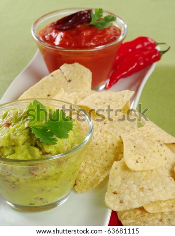 Guacamole with tacos and tomato-chili dip and chilies in the background on green (Selective Focus, Focus on the Guacamole)