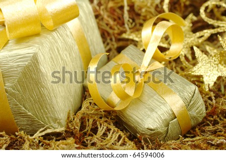 Boxes wrapped in golden paper with golden ribbon on brown moss (Selective Focus, Focus on front of the small box)