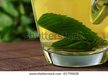 Fresh mint tea with mint leaves in glass cup on wooden place mat with mint leaves in the background (Selective Focus, Focus on parts of the leaves in the cup)