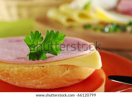 Open sandwich with a cold meat slice and cheese slice with parsley on top on orange plate with knife, and ingredients in the background (Selective Focus, Focus on the front of the sandwich)