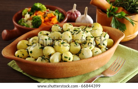 Small potatoes with herbs, such as parsley, thyme and rosemary with vegetables, garlic and a mortar with herbs in the background (Selective Focus, Focus on the front of the potatoes and the bowl)