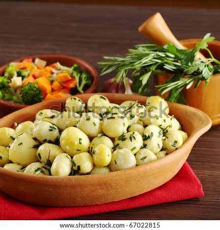 Small potatoes with herbs, such as parsley, thyme and rosemary with fried vegetables and a mortar with herbs in the background (Selective Focus, Focus on the front of the potatoes and the bowl)