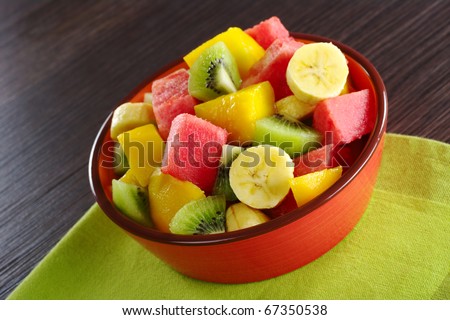 Fresh fruit salad made of banana, kiwi, watermelon and mango pieces in orange bowl (Selective Focus, Focus on the front of the bowl and the fruits in the front)