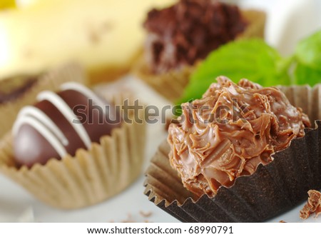 Chocolate truffles with mint leaf, fine chocolate shavings and a yellow cake in the background (Very Shallow Depth of Field, Focus on the front of the first truffle)