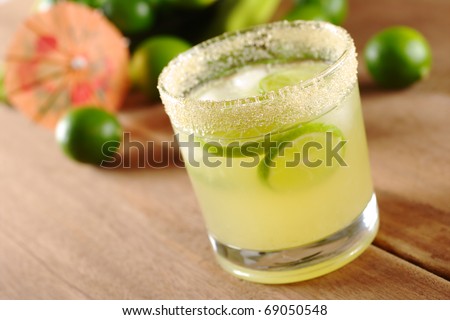 Fresh lemonade of green limes in sugar-rimmed glass on wooden board with limes and an orange paper sunshade in the background (Selective Focus, Focus on the front of the rim of the glass)