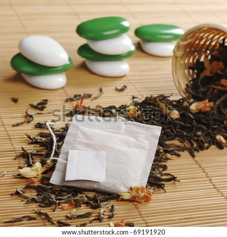 Teabag with empty label on lose green tea with dried jasmine blossoms and a wooden tea strainer and some white and green stones in the background (Selective Focus, Focus on the teabag and the label)