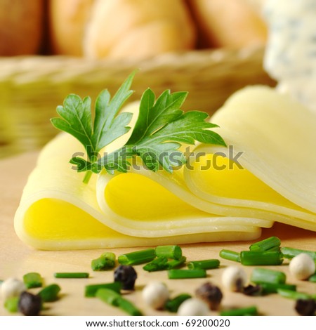 Cheese slices and parsley with chives and pepper corns in the front and bread basket in the back (Selective Focus, Focus on the front of the cheese slices and the parsley)