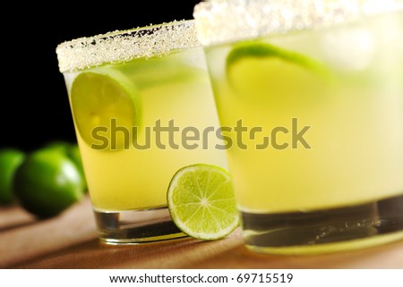 Fresh lemonade with lime and ice cubes in a sugar rimmed glass on wood with limes in back on black background (Very Shallow Depth of Field, Focus on the glass in the back and the lime slice before it)