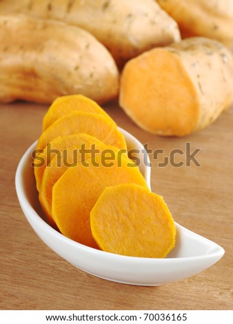 Cooked sweet potato (lat. Ipomoea batatas) cut in slices in white bowl on wooden surface with sweet potatoes in the background (Selective Focus, Focus on the front of the bowl)