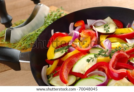The raw ingredients (zucchini, bell pepper, onion, eggplant) of ratatouille in a frying pan with thyme on top and in the background (Selective Focus, Focus on the thyme sprig in the frying pan)