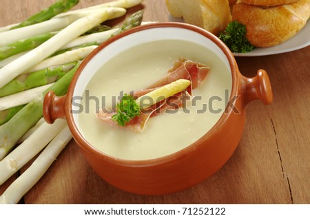 Asparagus soup garnished with ham, asparagus head and parsley accompanied by bread with raw asparagus lying by the side (Selective Focus, Focus on the garnish on the top of the soup)