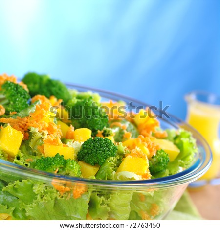 Broccoli-mango-carrot-lettuce salad in a glass bowl with orange juice dressing in the background (Selective Focus, Focus on the front)
