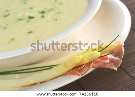 Cream of white asparagus garnished with parsley and white asparagus, ham and chives on the rim (Selective Focus, Focus on the front of the asparagus heads and ham)
