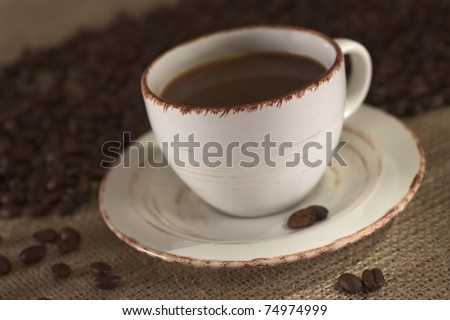 Hot fresh coffee in cup surrounded by coffee beans (Very Shallow Depth of Field, Focus on the front of the rim)