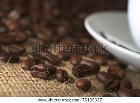 Coffee beans on fabric called Jute with a saucer and a coffee cup on the side (Very Shallow Depth of Field, Focus on the coffee bean on the left which is lit the most)