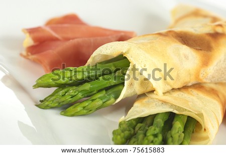 Green asparagus wrapped in crepes with ham in the background (Selective Focus, Focus on the horizontal asparagus heads)