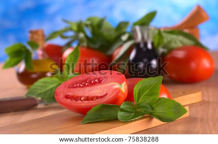 Fresh basil leaves with tomato halves with mortar, tomato, basil leaves, balsamic vinegar and olive oil in the back (Selective Focus, Focus on the basil in front)