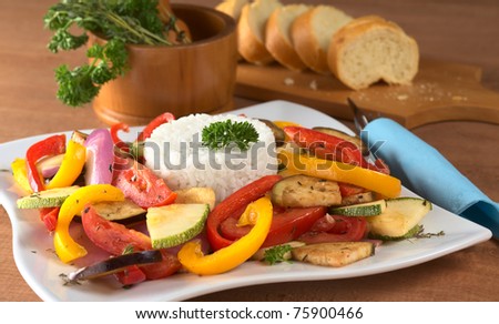 Ratatouille of zucchini, eggplant, tomato, bell pepper and onion with cooked rice and mortar with herbs, baguette in the back (Selective Focus, Focus on the front of the rice and the vegetable around)