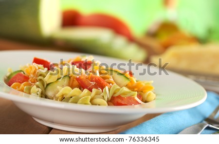 Colorful fusilli pasta with zucchini, tomato and grated cheese with fork on the side and ingredients in the back (Selective Focus, Focus one third into the meal)