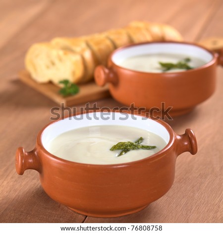 Cream of asparagus with green asparagus heads in rustic bowl with slices of baguette white bread in the back on wood (Selective Focus, Focus on the asparagus head in the first bowl)
