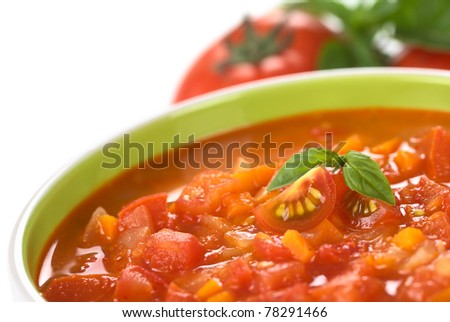 Chunky tomato soup made of tomatoes, carrots and onions and garnished with cherry tomato and a basil leaf (Selective Focus, Focus on the left cherry tomato and the right basil leaf)