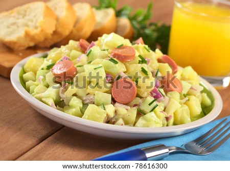 Fresh potato salad made of potato, cucumber, red onion and chives with mayonnaise dressing and sausage slices (Selective Focus, Focus one third into the salad, on the sausage slice in the middle)