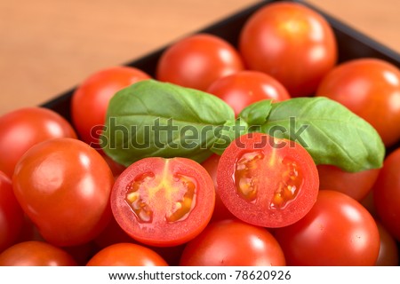 Cherry tomatoes with basil leaf in a black bowl (Selective Focus, Focus on the right tomato half)