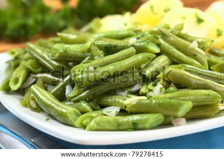 Cooked green beans with onion and parsley with cooked potato in the back (Selective Focus, Focus one third into the beans)