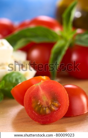 Raw cherry tomato cut in half with cheese and basil in the back (Selective Focus, Focus on the surface of the cut tomato)