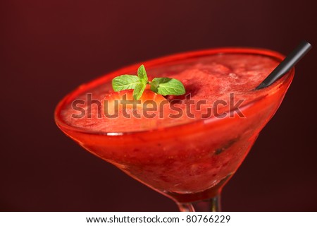 Frozen Strawberry Daiquiri in a cocktail glass with a strawberry slice and a mint leaf on the drink and a black straw on the side (Selective Focus, Focus on the strawberry and the front of the mint)