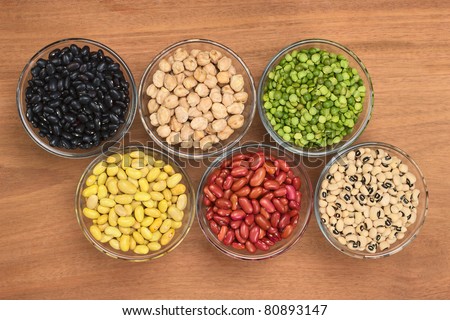 A variety of legumes (black beans, chickpeas, slit peas, canary beans, kidney beans and black-eyed peas) in glass bowl photographed on wood from above