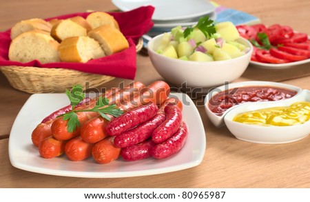 Two types of sausages with ketchup, mustard, potato salad, baguette and tomato slices (Selective Focus, Focus on the front of the sausages)