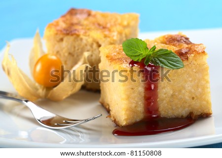 Baked rice pudding dessert with strawberry sauce and a mint leaf (Selective Focus, Focus on the front left edge of the cake, the strawberry sauce and the front of the mint)