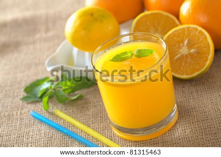 Freshly squeezed orange juice with orange slice and mint leaf on top of the juice (Selective Focus, Focus on the mint leaf on top of the juice)
