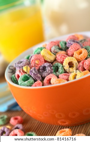 Colorful cereal rings in orange bowl with orange juice and milk in the back (Selective Focus, Focus one third into the bowl)