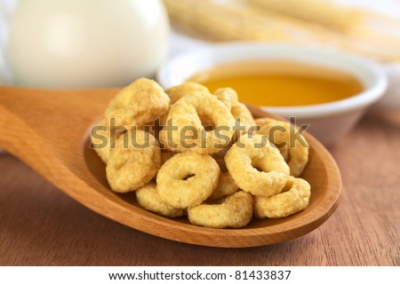 Honey flavored cereal loops on wooden spoon with milk and honey in the back (Selective Focus, Focus on the front of the loops in the front)