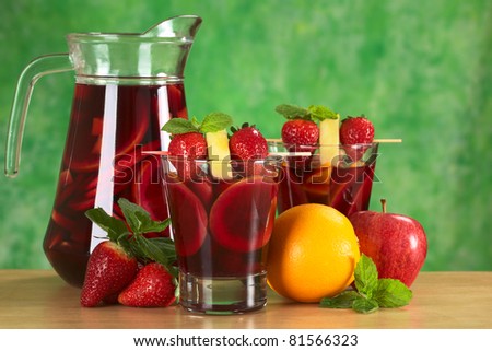Red wine punch called sangria mixed orange, apple and mango, garnished with strawberries and pineapple with a jug of sangria and fruits (Selective Focus, Focus on the fruits on the skewer in front)