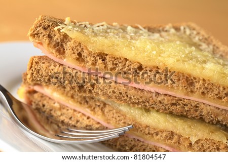 Croque Monsieur. Baked wholewheat bread sandwich filled with ham and cheese, grated cheese on top cut into two halves lying upon each other (Selective Focus, Focus on the upper edge of the upper half)