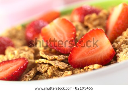 Wholewheat flakes with fresh strawberry halves with a glass of strawberry yogurt in the back (Selective Focus, Focus on the strawberry half in the right bottom corner)