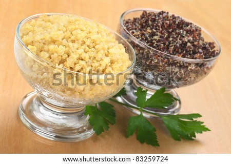 Cooked white and red quinoa in glass bowls which can be eaten as a side dish like rice and is rich in proteins with a parsley leaf on wood (Selective Focus, Focus on the front of the white quinoa)