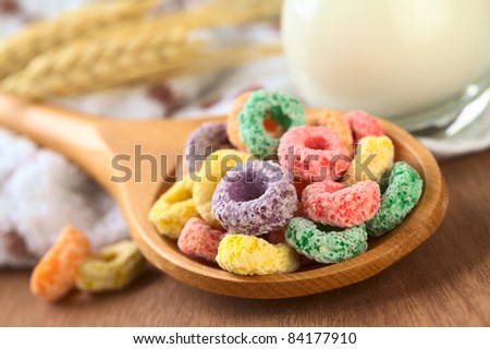 Colorful cereal loops with different fruit flavor on wooden spoon with some milk in the back (Selective Focus, Focus on the rings in the front)